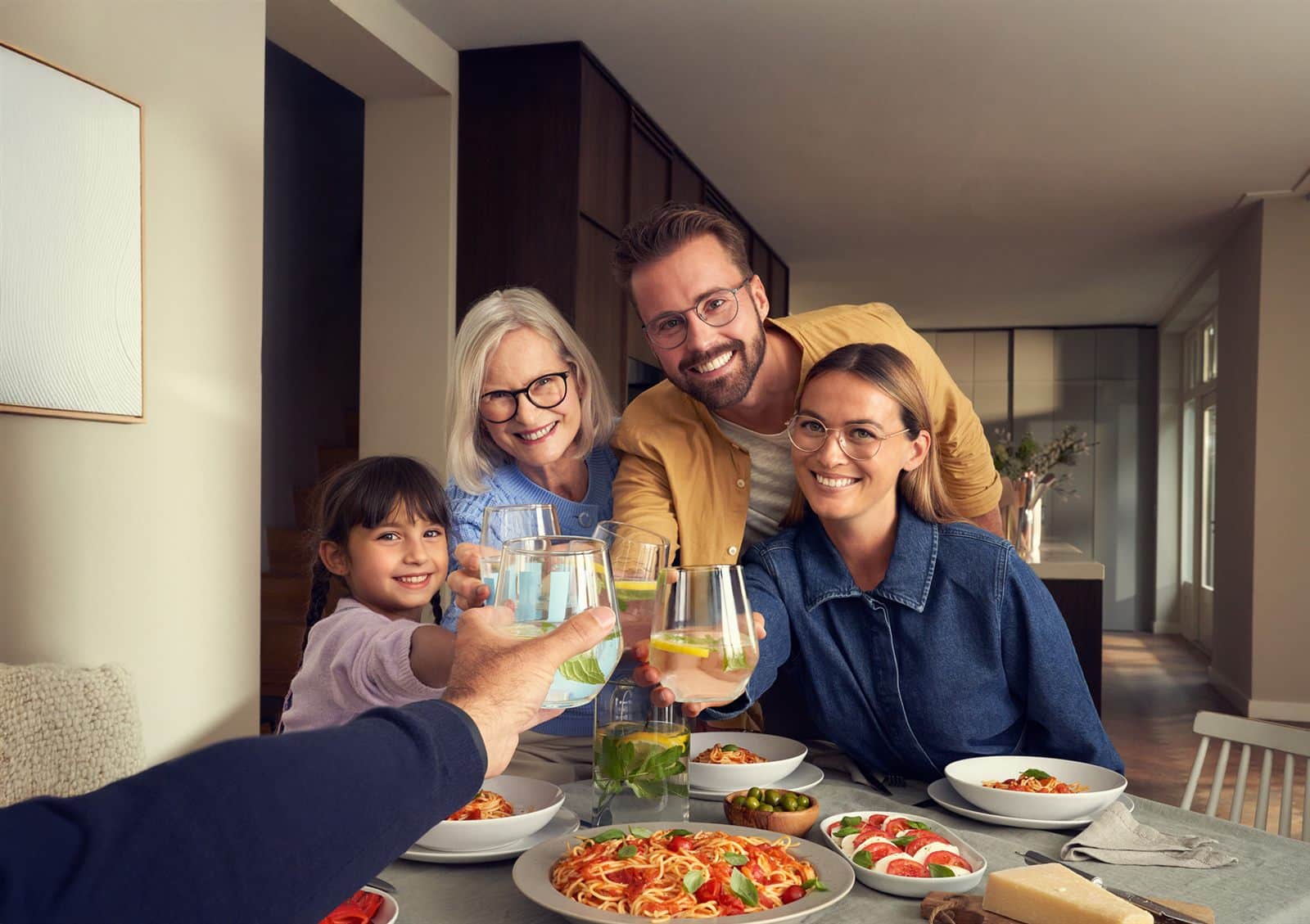 Une famille de quatre générations trinque autour d’une table, chacun porte des lunettes